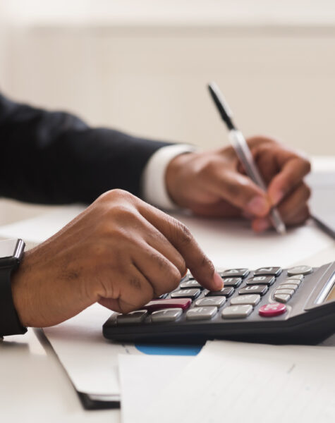 Accounting consulting concept. Businessman checking on incomes in office, using calculator, taking notes, cropped