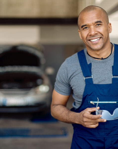 Portrait of happy black mechanic working in auto repair shop and looking at camera.