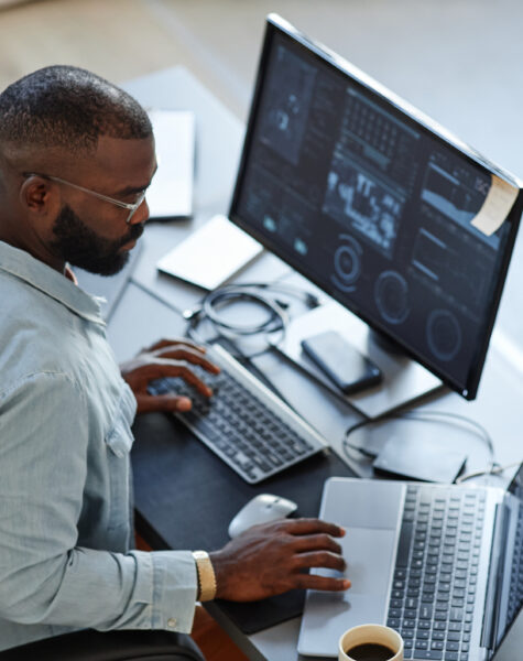 Minimal high angle view at African American software developer working with computers and data systems in office