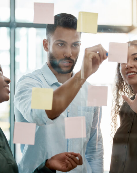 Team strategy meeting on research, post it on glass wall and group work planning together. Business people brainstorming analytics vision think tank ideas, collaboration thinking and sticky notes